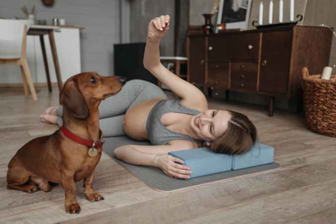 a pregnant woman lying over a yoga mat besides her dog